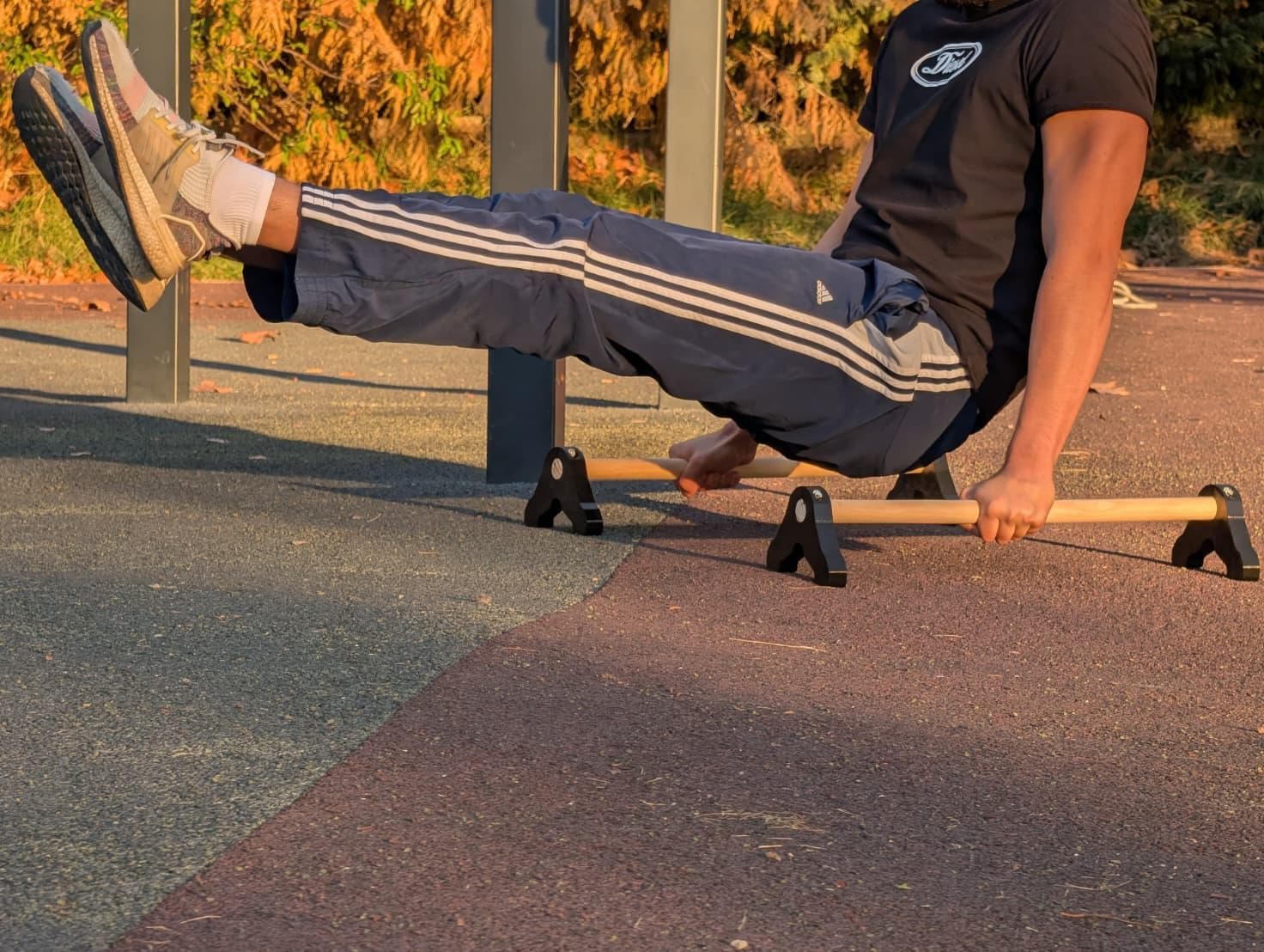 L-sit con las piernas elevadas sobre paralelas de madera, luz cálida de tarde